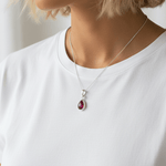 Person wearing a sterling silver necklace with a teardrop-shaped pendant featuring a red  ruby gemstone.