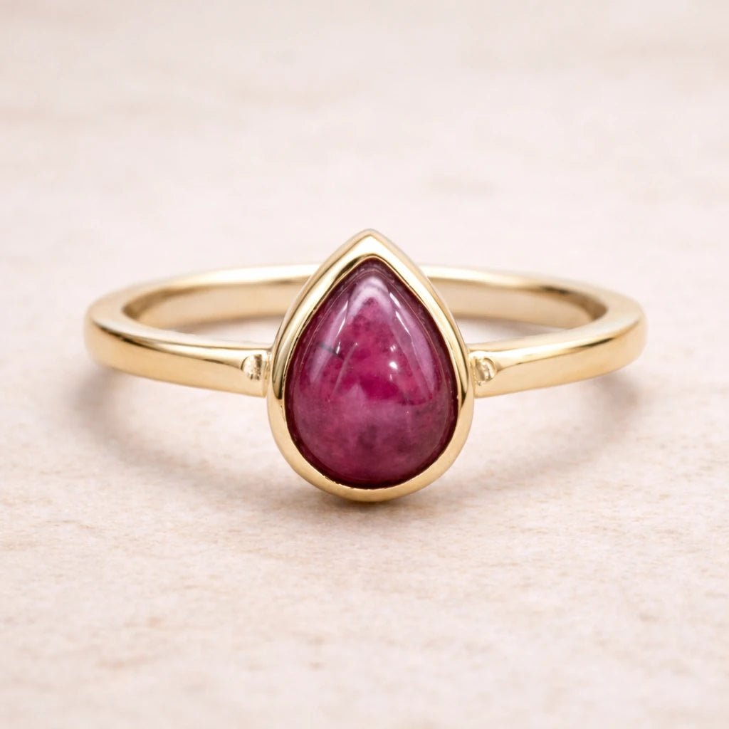 Gold ring with a teardrop-shaped natural ruby gemstone on a beige background
