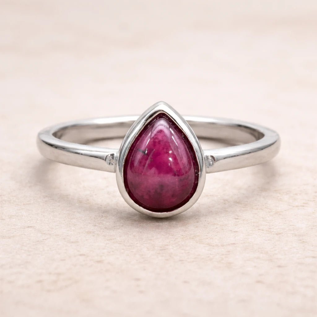 Silver ring with a teardrop-shaped ruby stone on a beige background