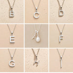 Collection of silver necklaces with initial pendant A to I on a beige background as personalised letter options to add to a June Birthstone Mother of Pearl Necklace.