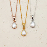 Three pearl pendant necklaces in gold, rose gold, and silver on a beige background