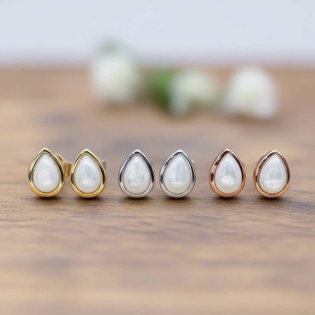 Set of six teardrop-shaped pearl earrings with silver, gold and rose gold settings on a wooden surface.
