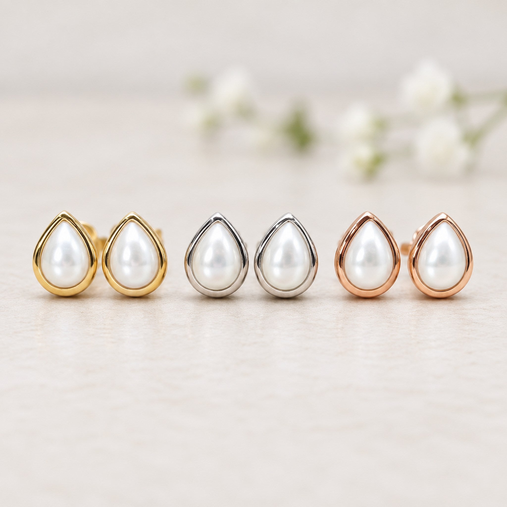 Set of six June birthstone pear-shaped pearl earrings with silver, gold and rose gold settings on a wooden surface.