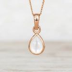Rose Gold necklace with a teardrop-shaped natural mother of pearl pendant hanging above a wooden table