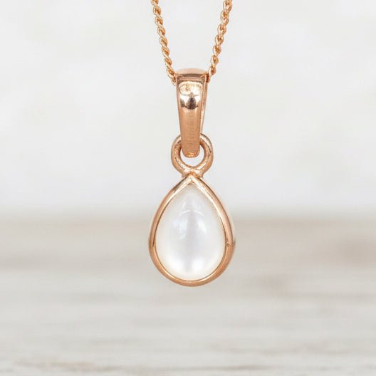 Rose Gold necklace with a teardrop-shaped natural mother of pearl pendant hanging above a wooden table