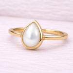 Gold ring with a teardrop-shaped pearl on a light pink background