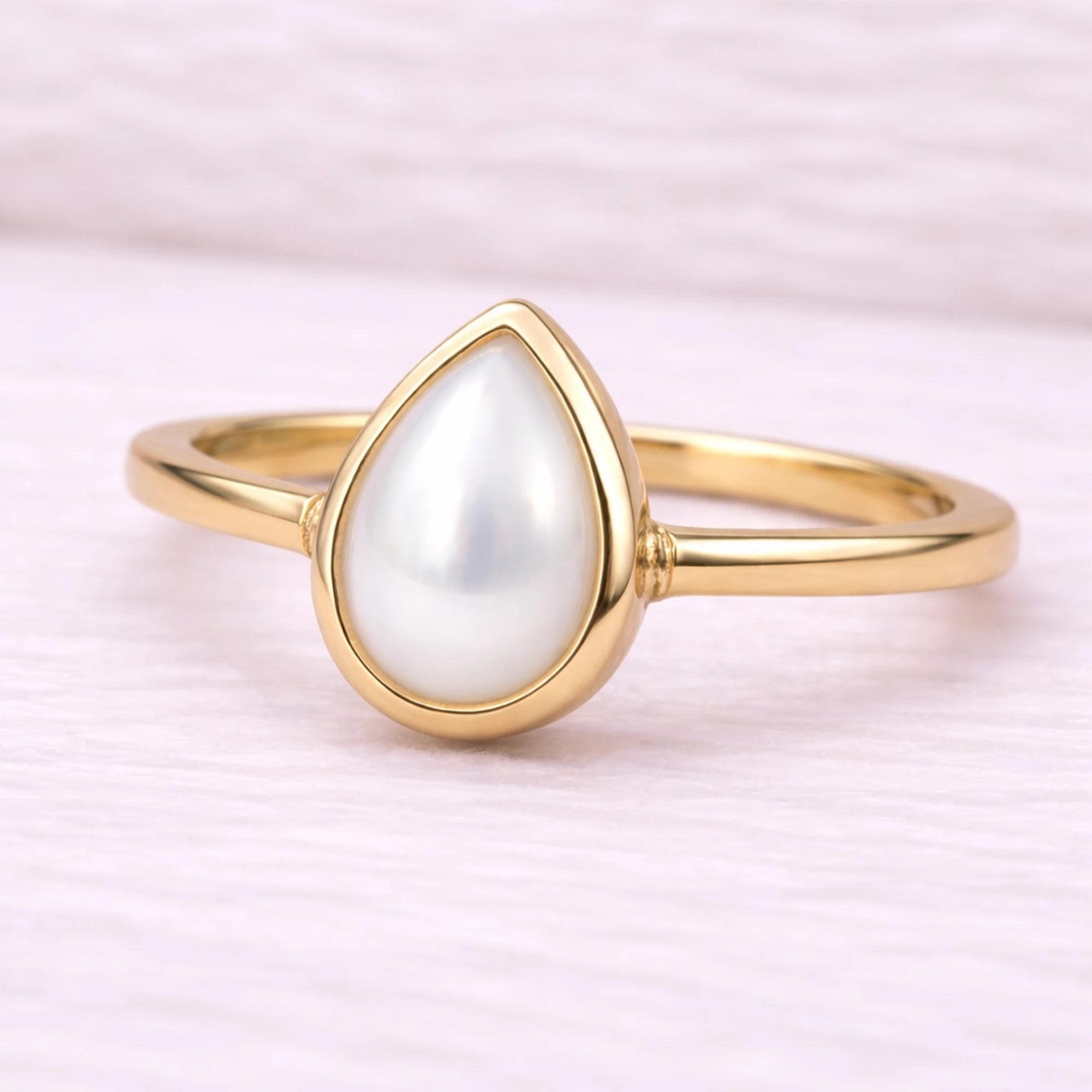 Gold ring with a teardrop-shaped pearl on a light pink background