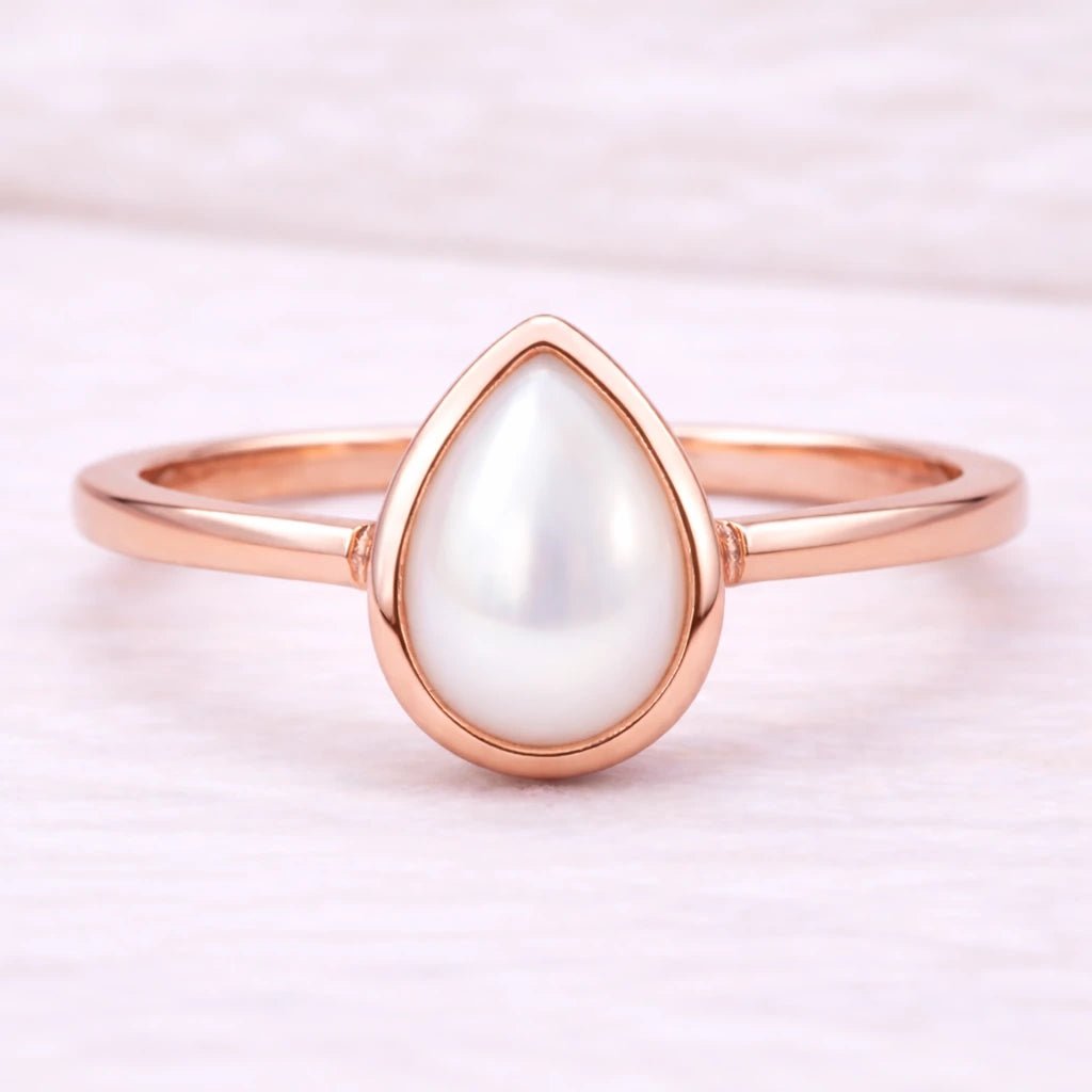 Rose gold ring with a teardrop-shaped pearl on a light pink background