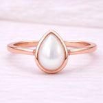 Rose gold ring with a teardrop-shaped pearl on a light pink background