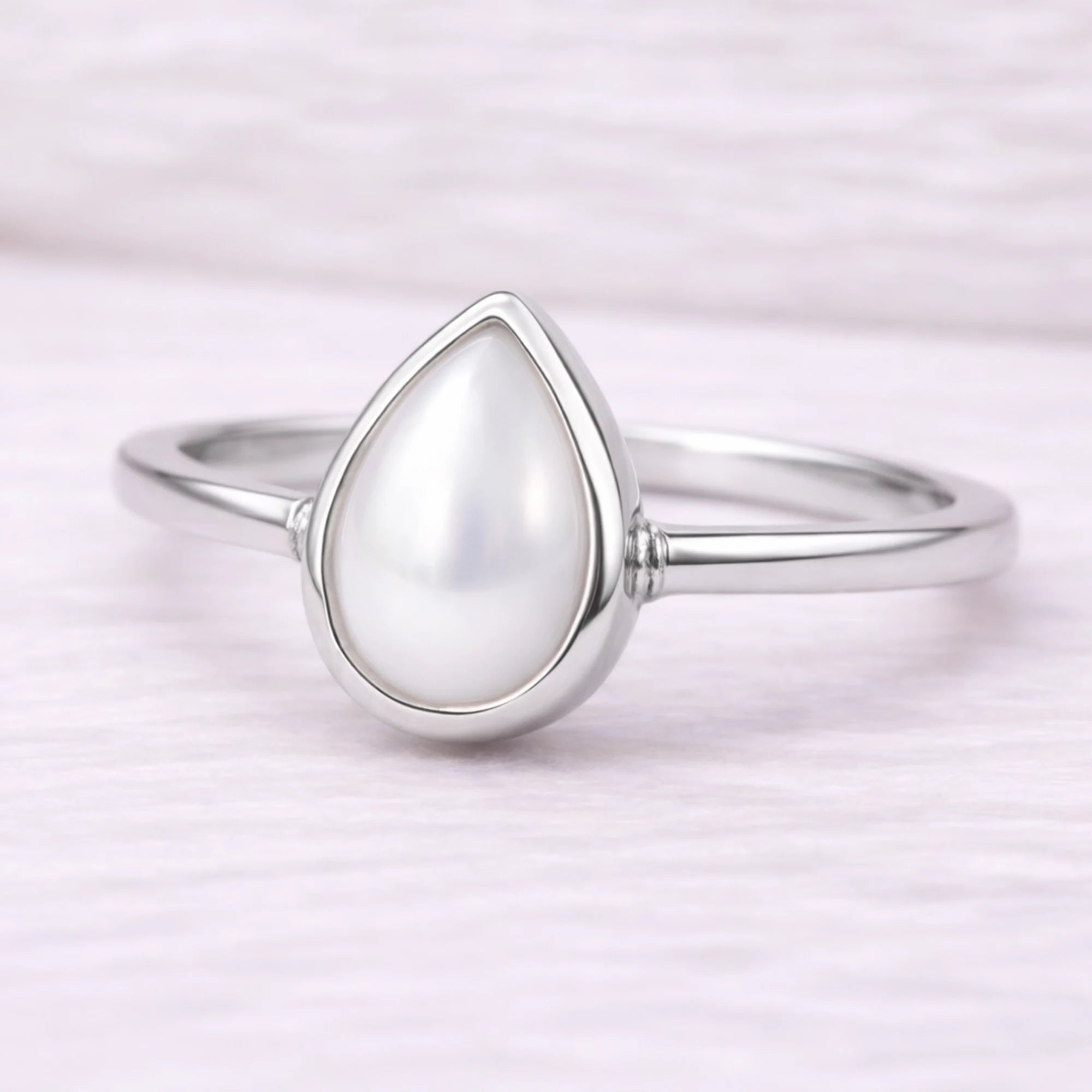 Silver ring with a teardrop-shaped pearl on a light pink background