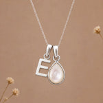 sterling silver initial e june birthstone natural mother of pearl pendant necklace against a dark warm beige background