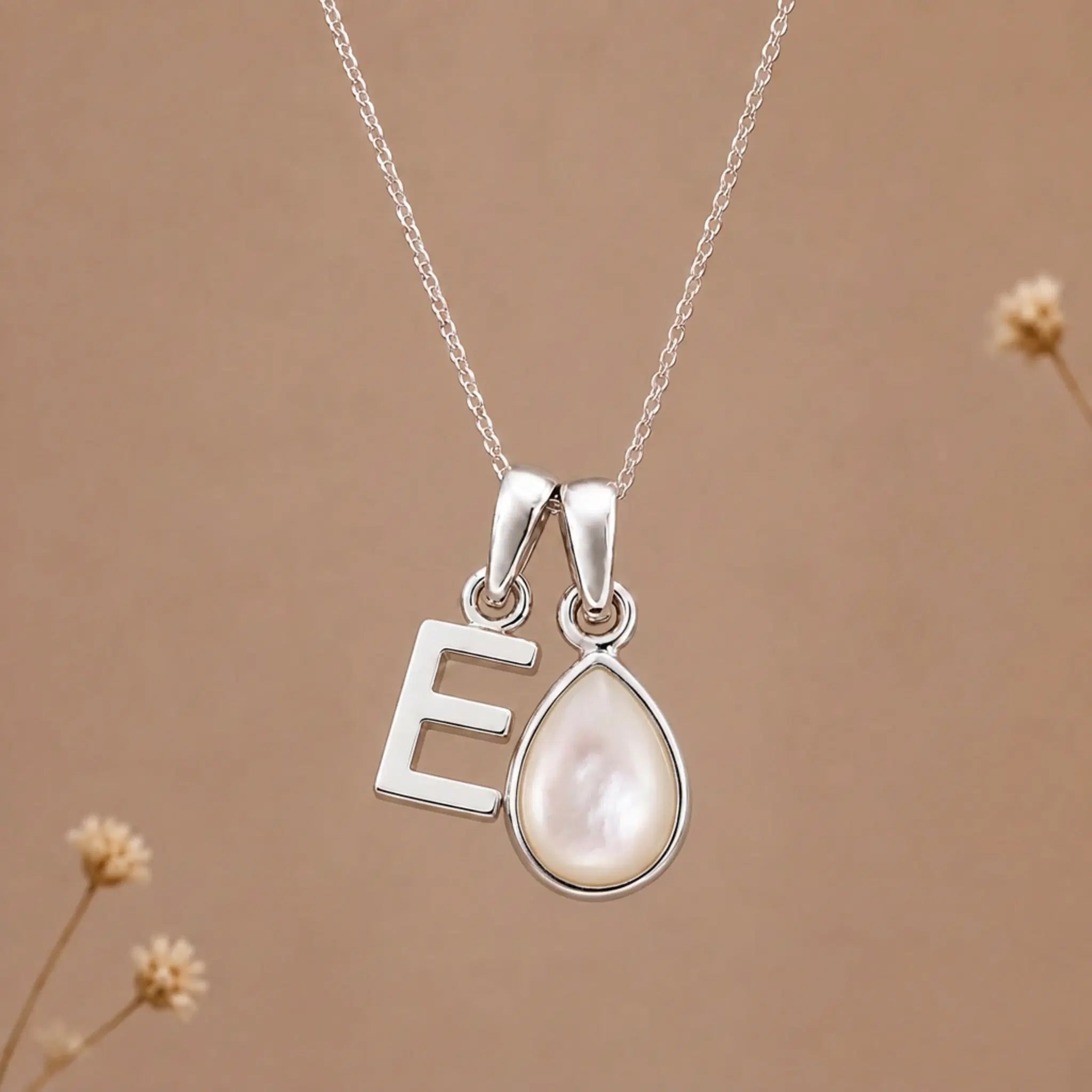 sterling silver initial e june birthstone natural mother of pearl pendant necklace against a dark warm beige background