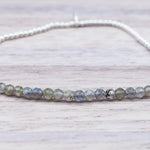 close up of a sterling Silver beaded bracelet with small faceted natural labradorite gemstone beads on a light wooden surface