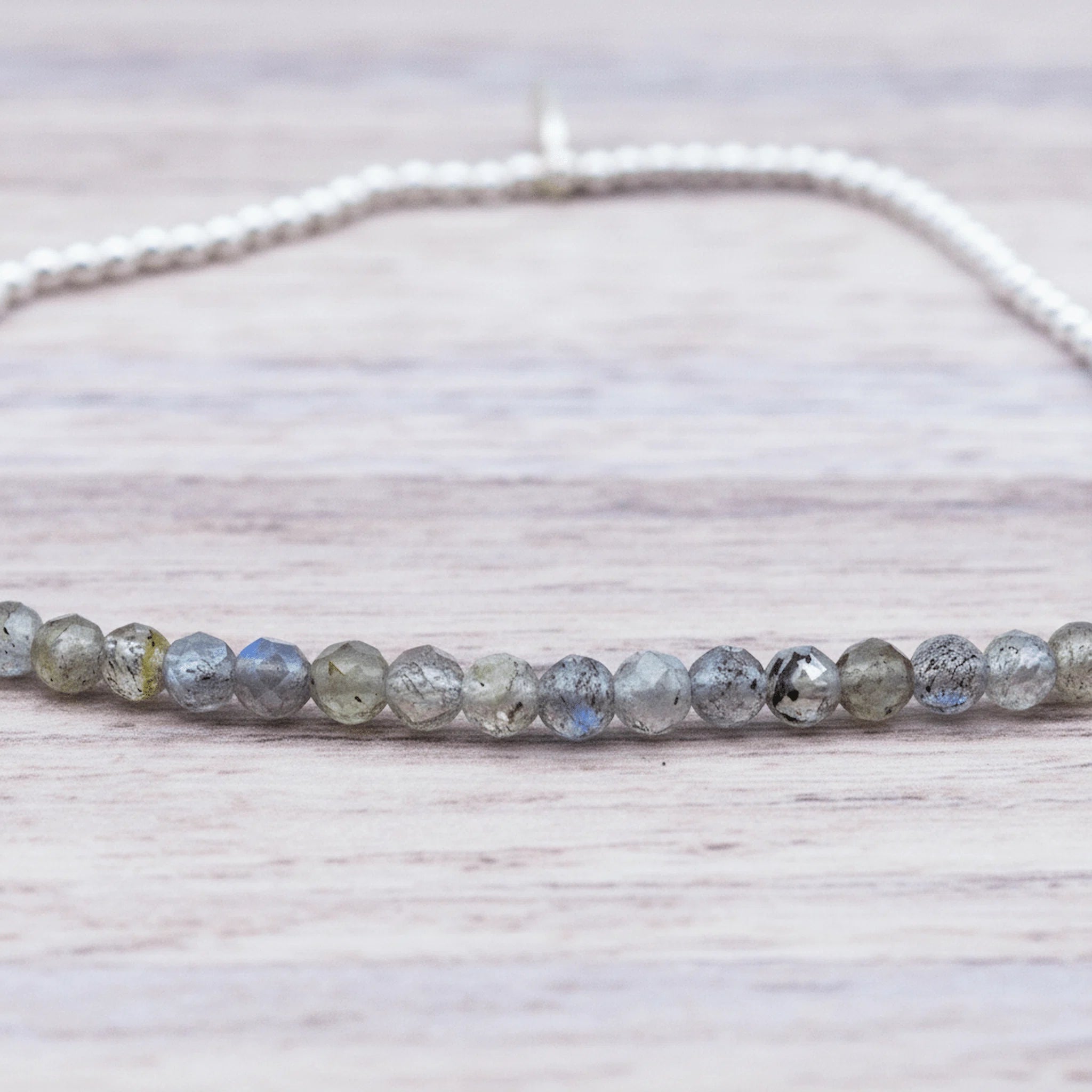 close up of a sterling Silver beaded bracelet with small faceted natural labradorite gemstone beads on a light wooden surface