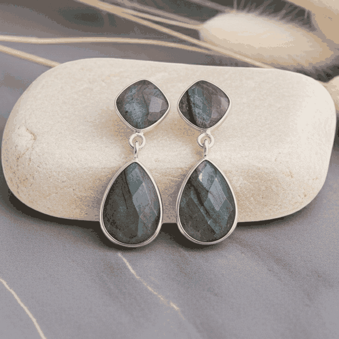 Teardrop-shaped earrings with green gemstones on a stone surface with dried grasses in the background