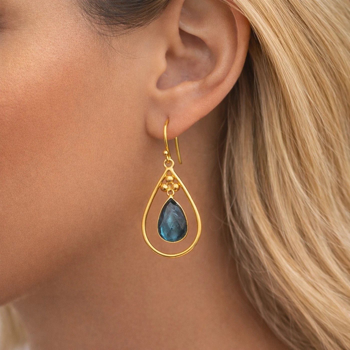 Gold earring with a labradorite gemstone worn by a person with blonde hair.