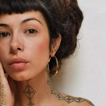 Woman with tattoos and large gold hoop earrings on a plain background