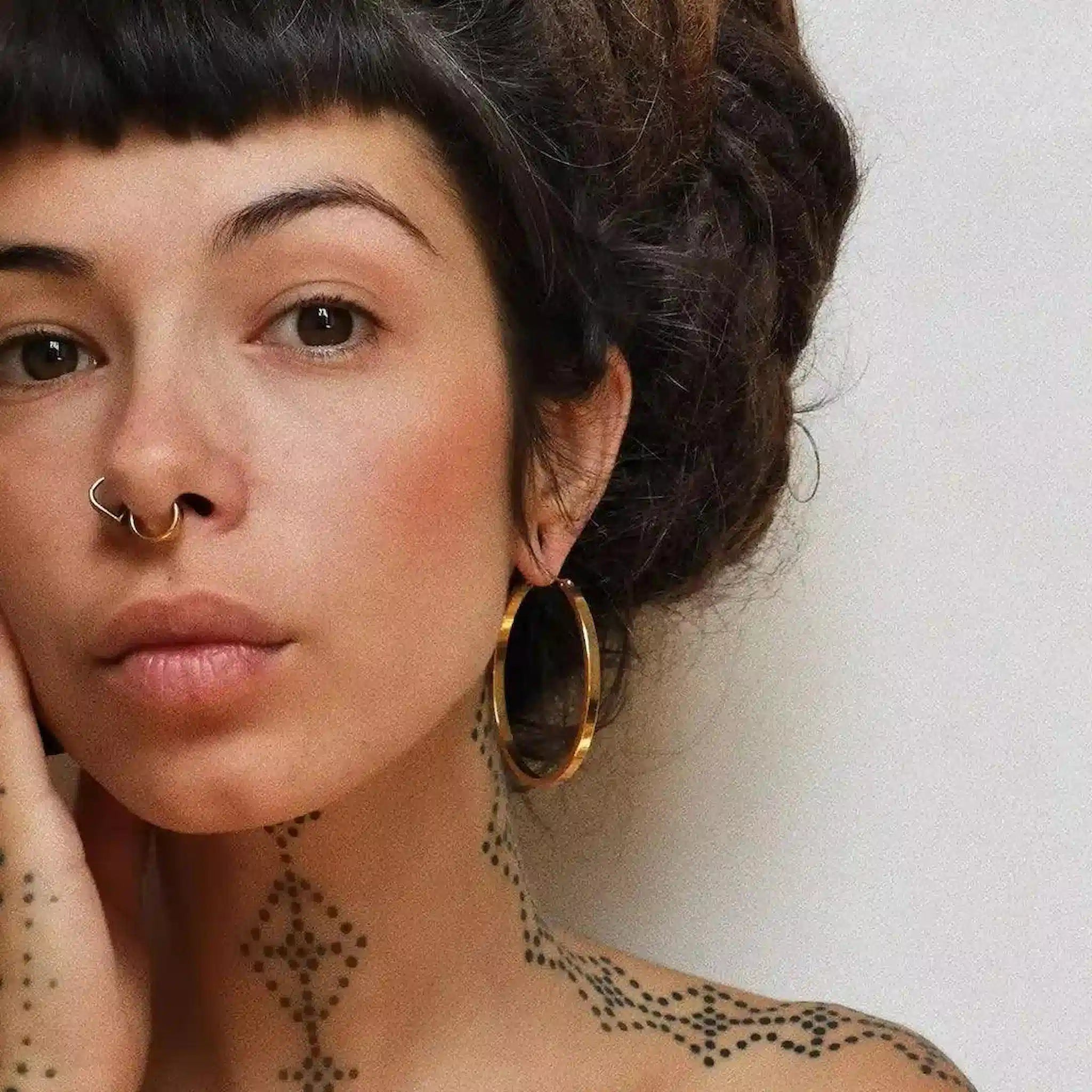 Woman with tattoos and large gold hoop earrings on a plain background