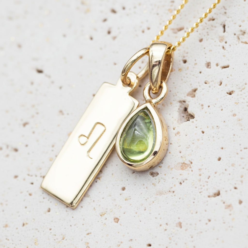 gold Leo zodiac pendant and August birthstone peridot pendant on a stone surface