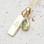 gold Leo zodiac pendant and August birthstone peridot pendant on a stone surface