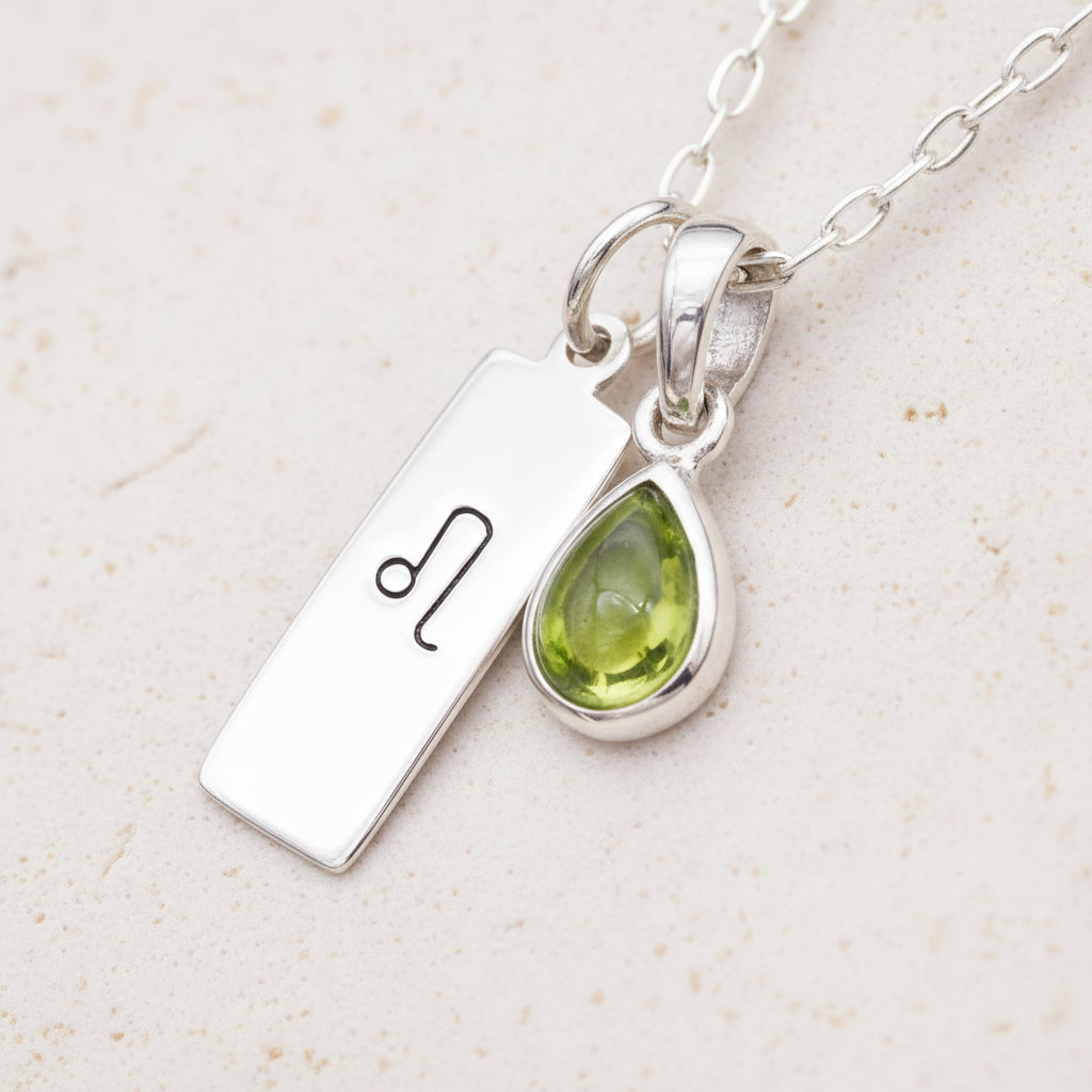Silver necklace with a green teardrop natural peridot pendant and a silver leo zodiac pendant on a textured surface