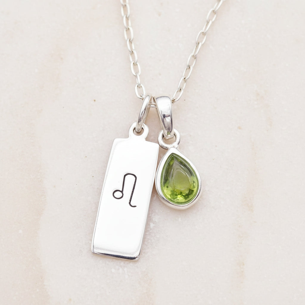 Sterling Silver necklace with a green teardrop natural Peridot gemstone pendant and a Leo Zodiac pendant on a textured surface.