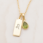 Gold necklace with a tag and a teardrop-shaped pendant on a light background