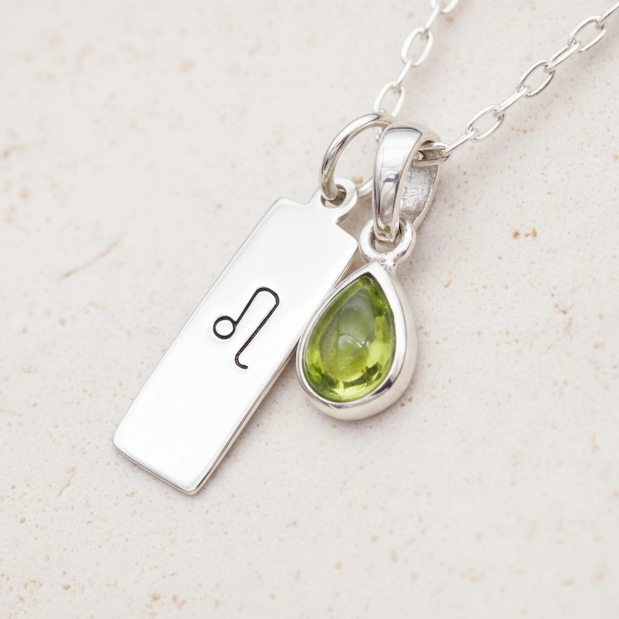 sterling silver Necklace with a leo zodiac pendant and a august birthstone peridot pendant on a light background
