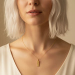 Close-up of a person wearing a gold necklace with a leo zodiac pendant against a neutral background