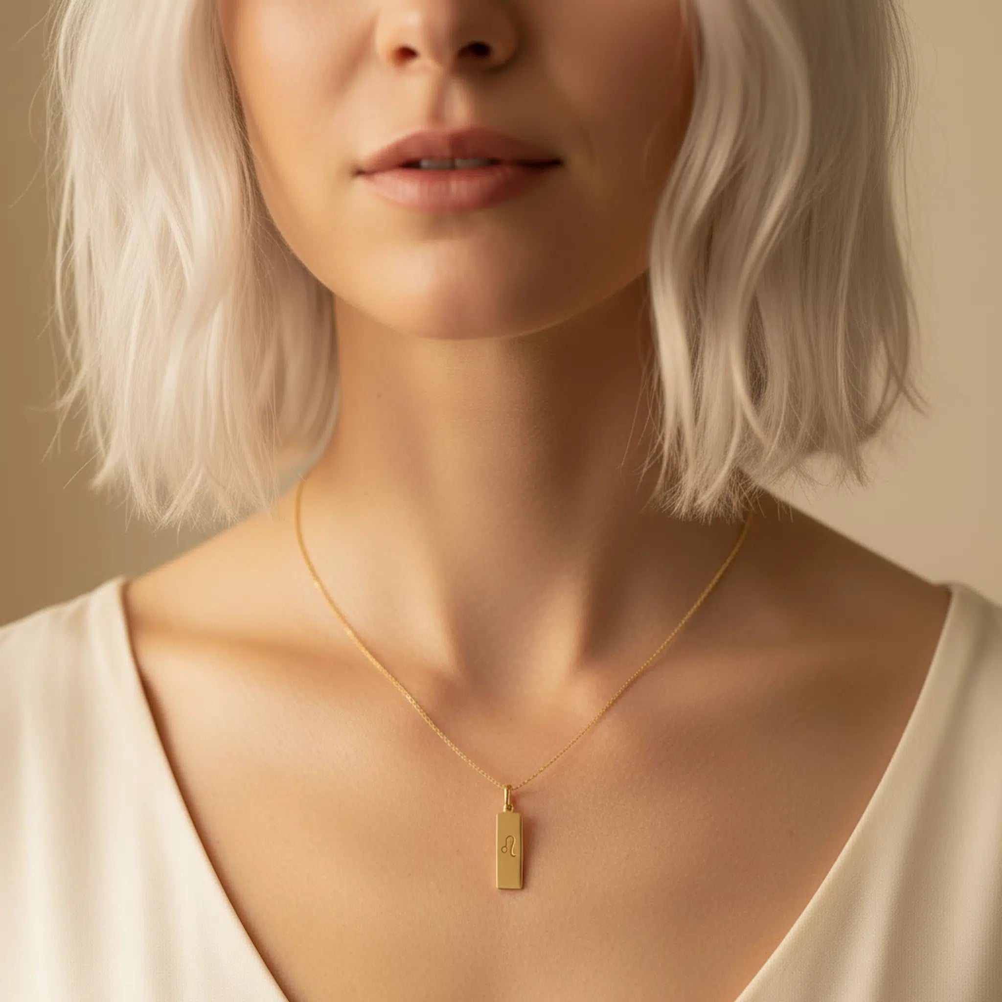 Close-up of a person wearing a gold necklace with a leo zodiac pendant against a neutral background