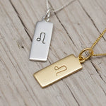 Gold and silver rectangular pendants with engraved leo zodiac symbols on a wooden surface
