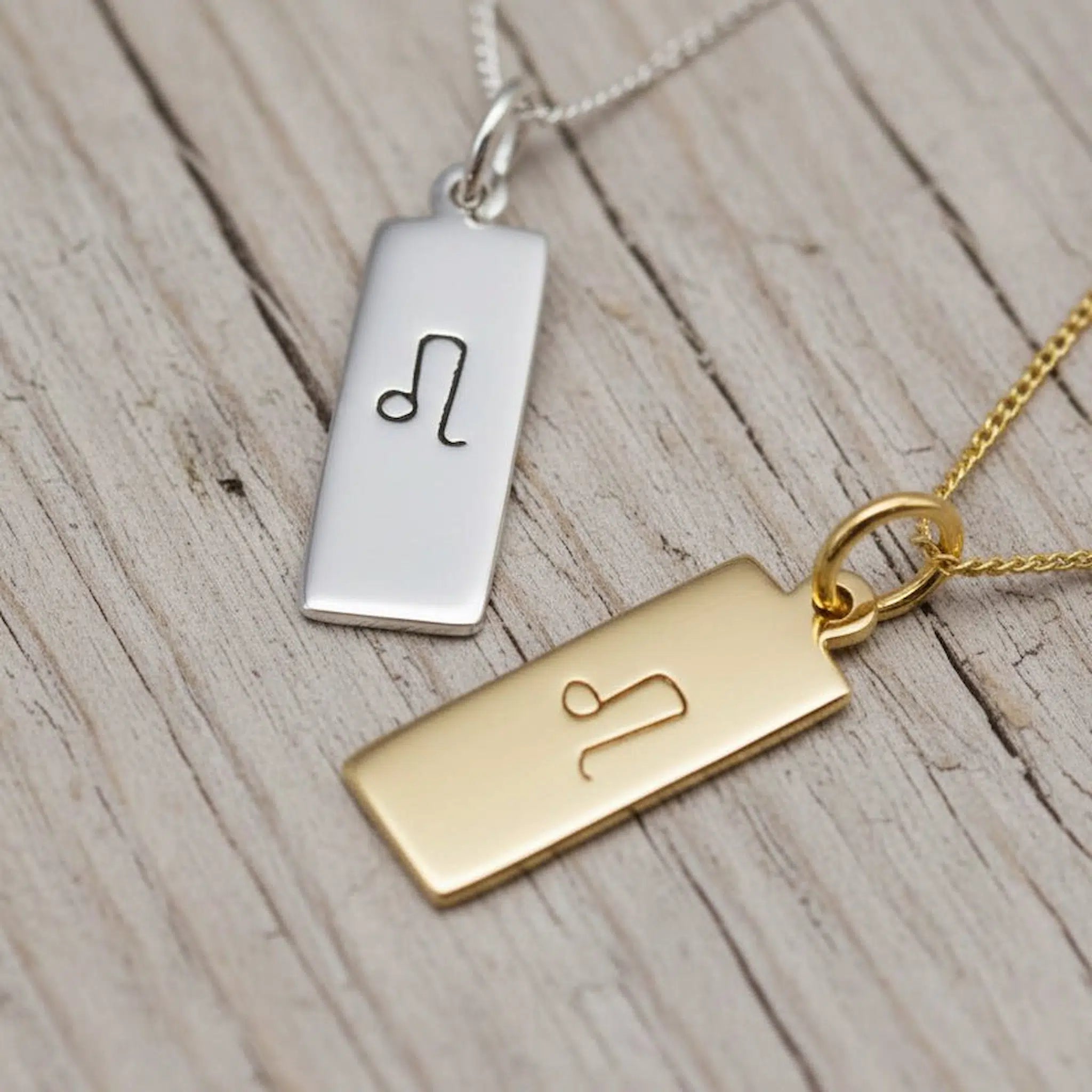 Gold and silver rectangular pendants with engraved leo zodiac symbols on a wooden surface