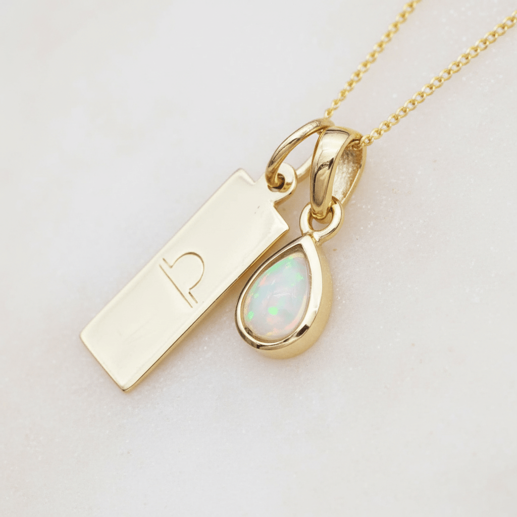 Gold Necklace with a libra zodiac pendant and pear shaped opal gemstone on a light stone surface