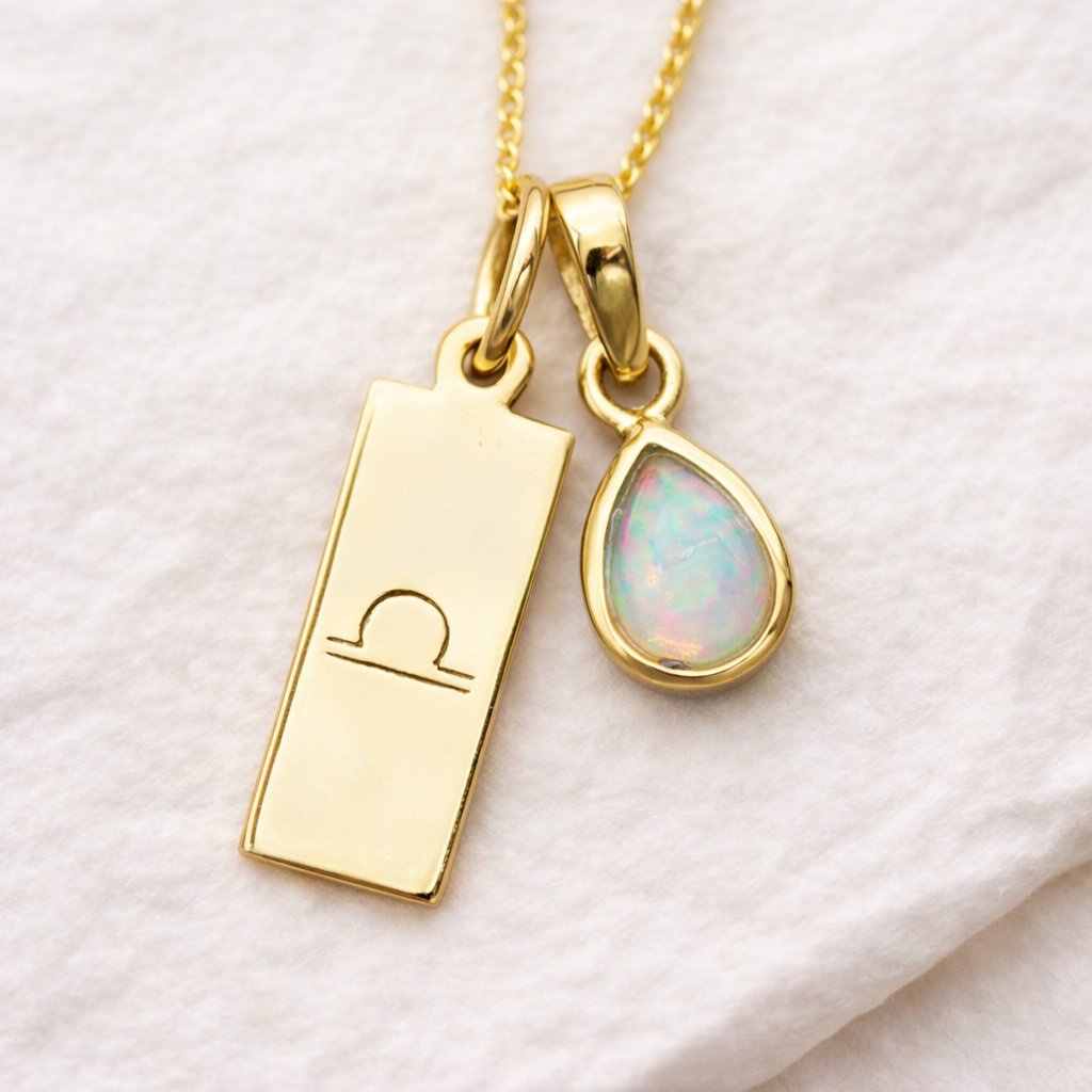 Gold necklace with libra zodiac sign pendant and opal teardrop charm on a white background