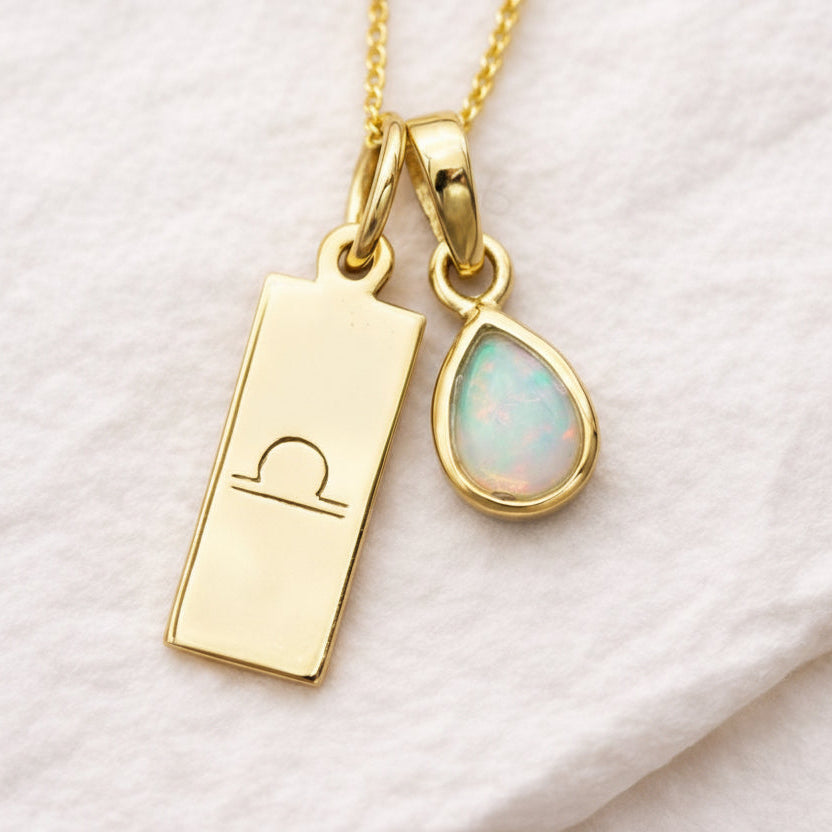 Gold necklace with libra zodiac sign pendant and opal teardrop charm on a white background