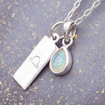 sterling silver necklace with a Libra zodiac pendant and October opal pendant on a stone surface