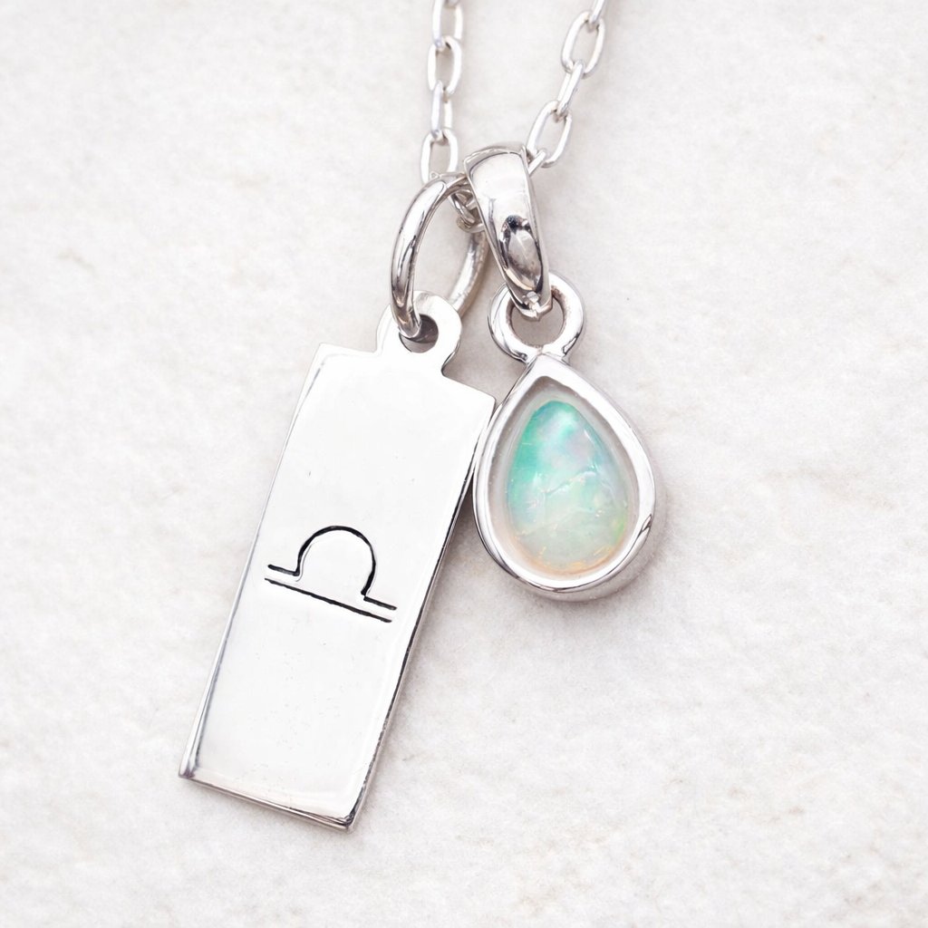 sterling Silver necklace with a rectangular libra zodiac pendant and teardrop-shaped opal pendant on a textured background.