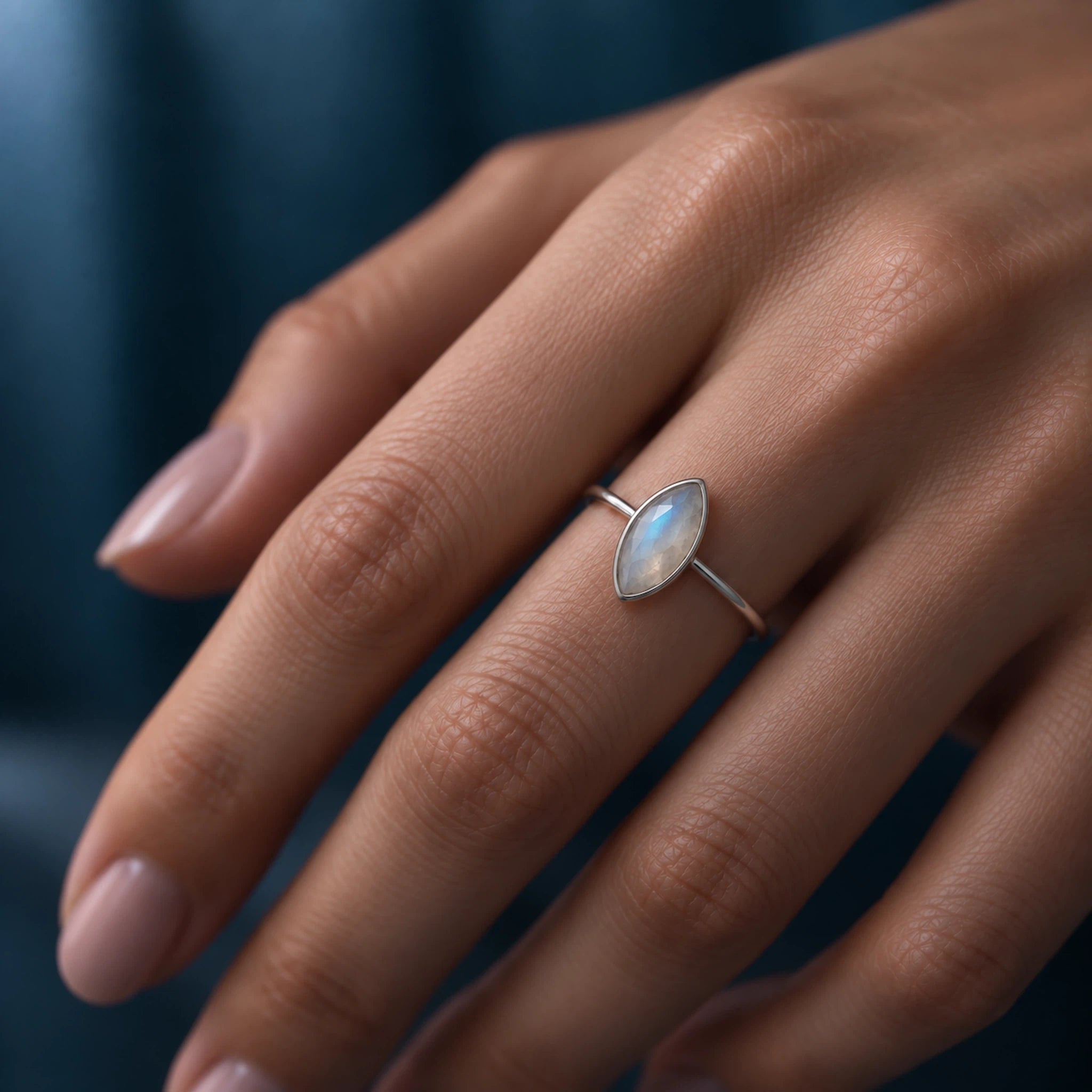 A close-up of a hand wearing a delicate silver ring with a marquise-cut iridescent moonstone.