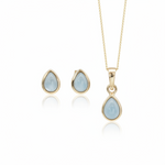 Gold jewelry set featuring a teardrop pendant necklace and matching stud earrings, each with a light blue teardrop gemstone in a gold bezel setting, shown on a white background with soft reflections.