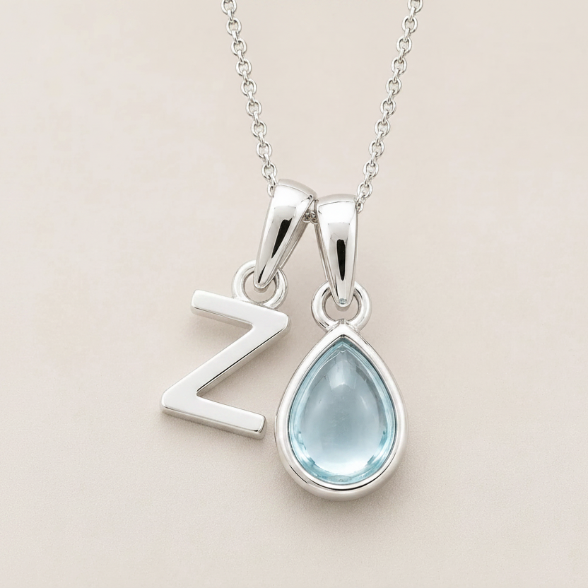 Sterling Silver double pendant necklace with a teardrop-shaped march birthstone aquamarine gemstone pendant and a Z letter pendant on a beige background