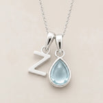 with a teardrop-shaped march birthstone aquamarine gemstone pendant and a Z letter pendant on a beige background
