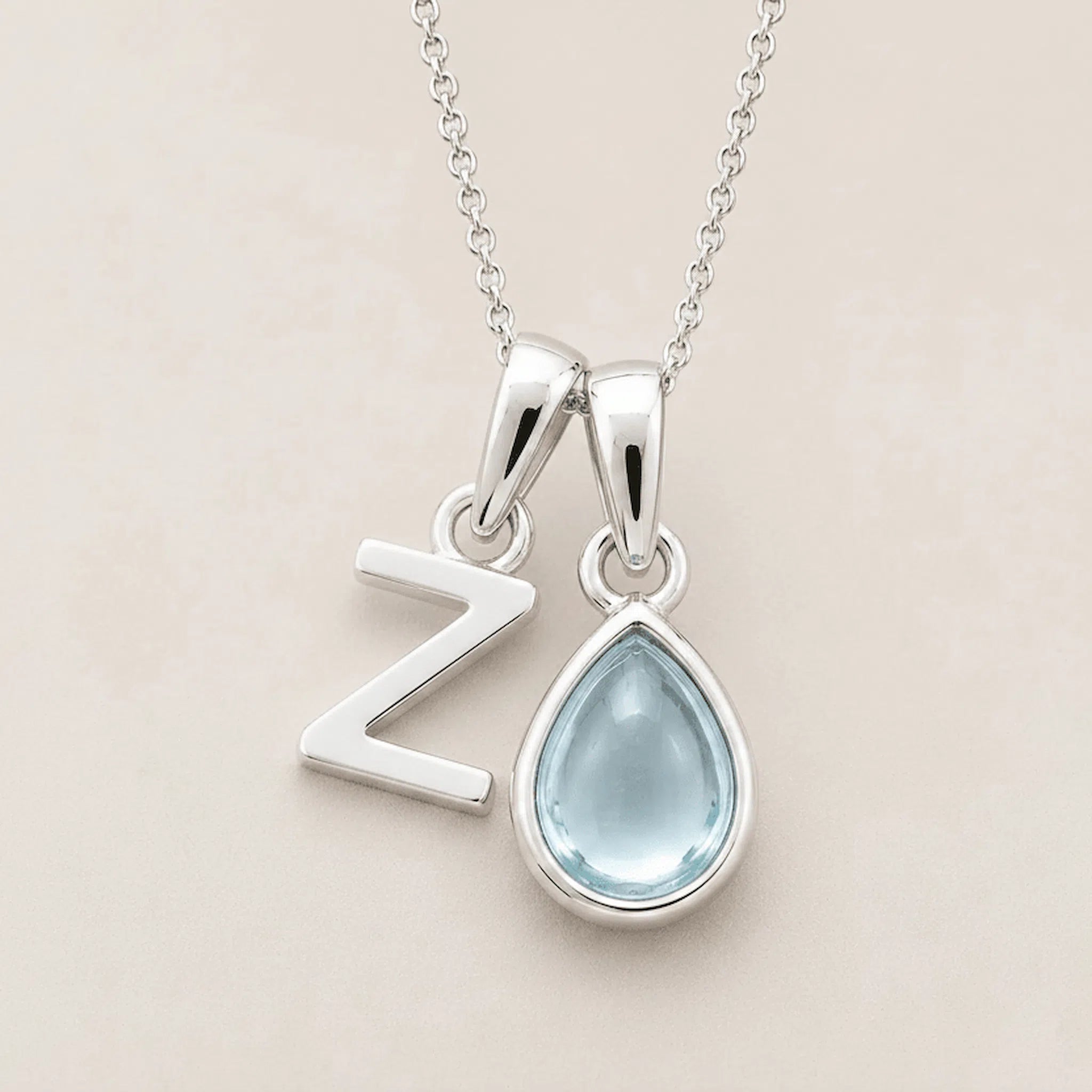 with a teardrop-shaped march birthstone aquamarine gemstone pendant and a Z letter pendant on a beige background