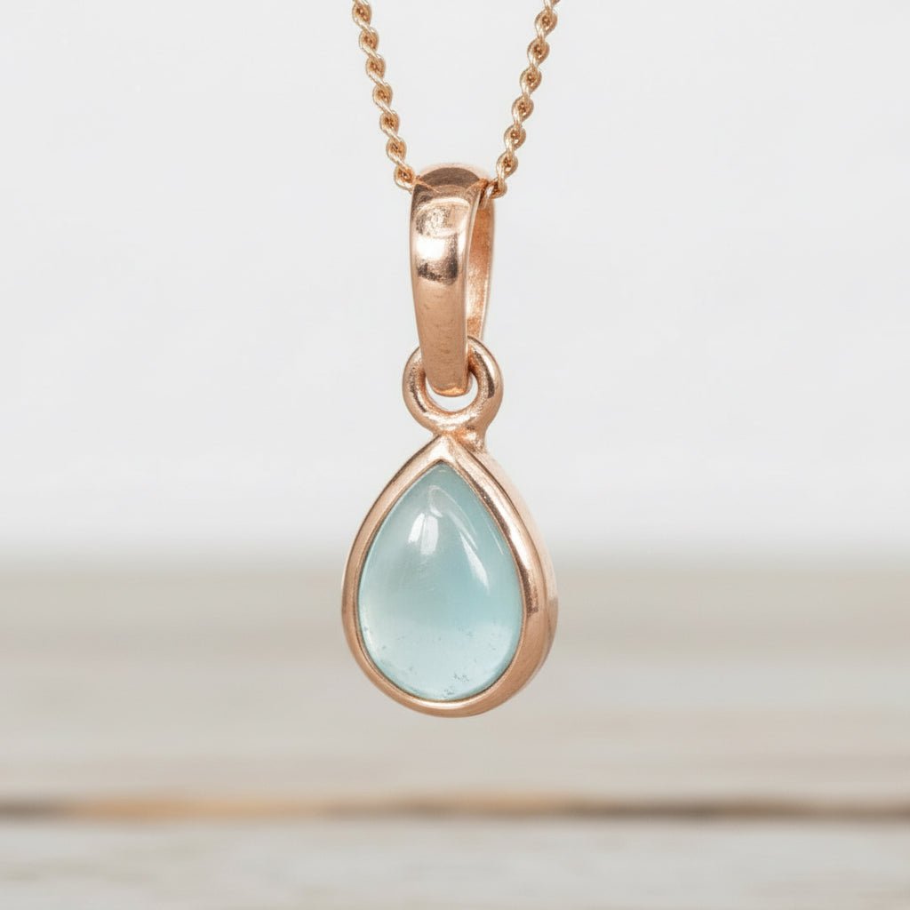 Rose gold pendant with a light blue aquamarine teardrop-shaped gemstone on a white background