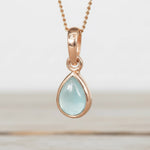 Rose gold pendant with a light blue aquamarine teardrop-shaped gemstone on a white background