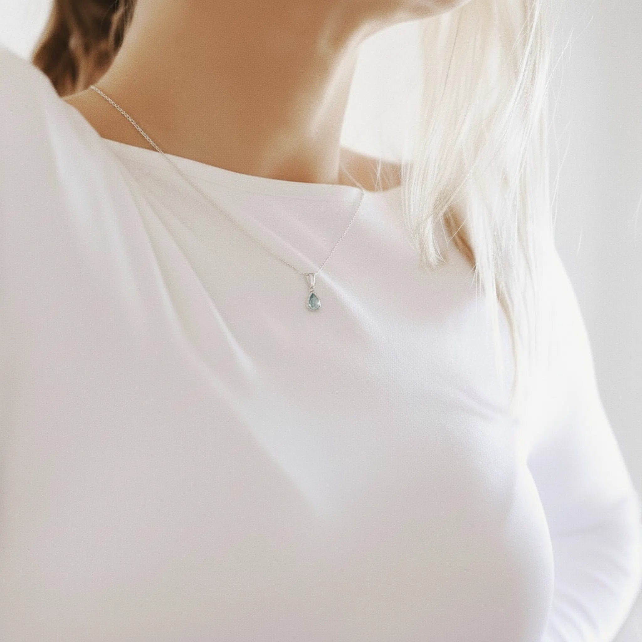 Close-up of woman wearing a sterling silver march birthstone necklace with a natural aquamarine gemstone pendant on a white background