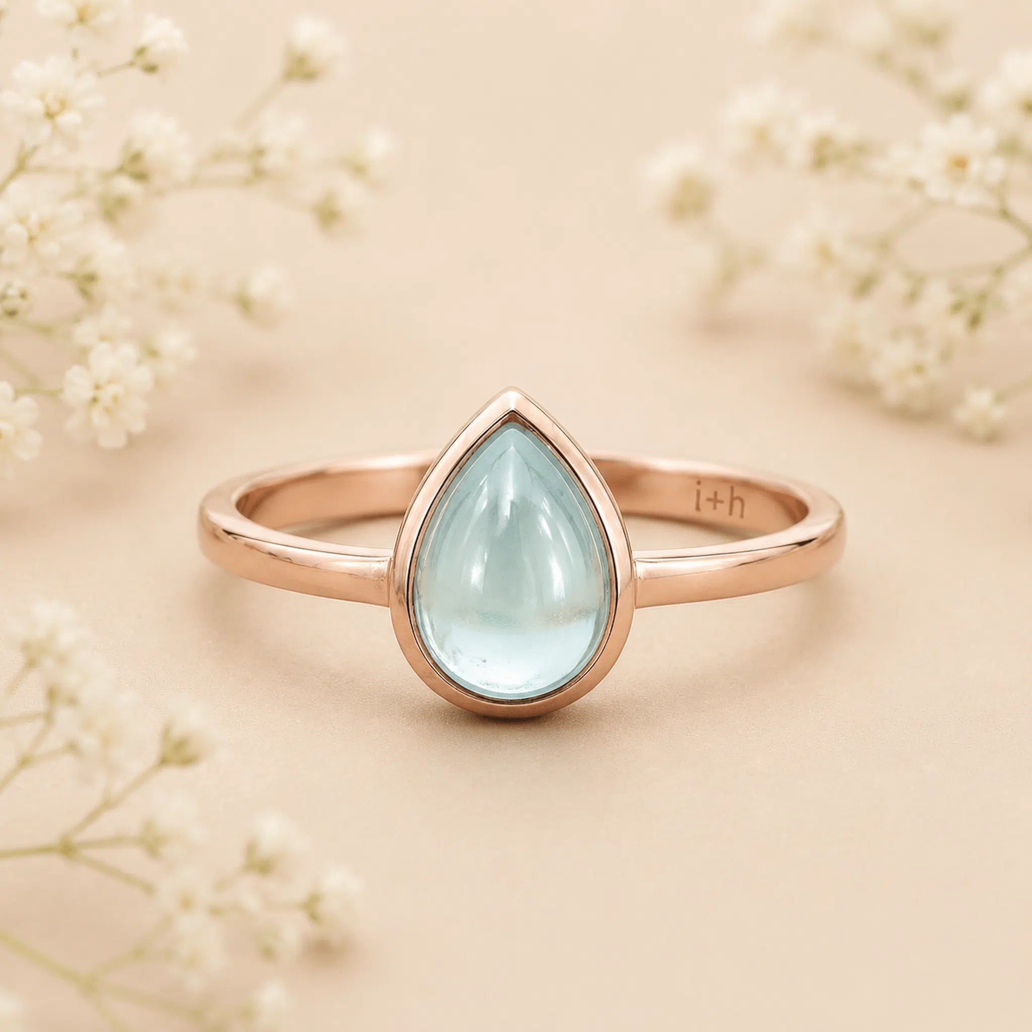 Rose gold March Birthstone ring with a teardrop-shaped light blue natural aquamarine gemstone on a wooden surface.