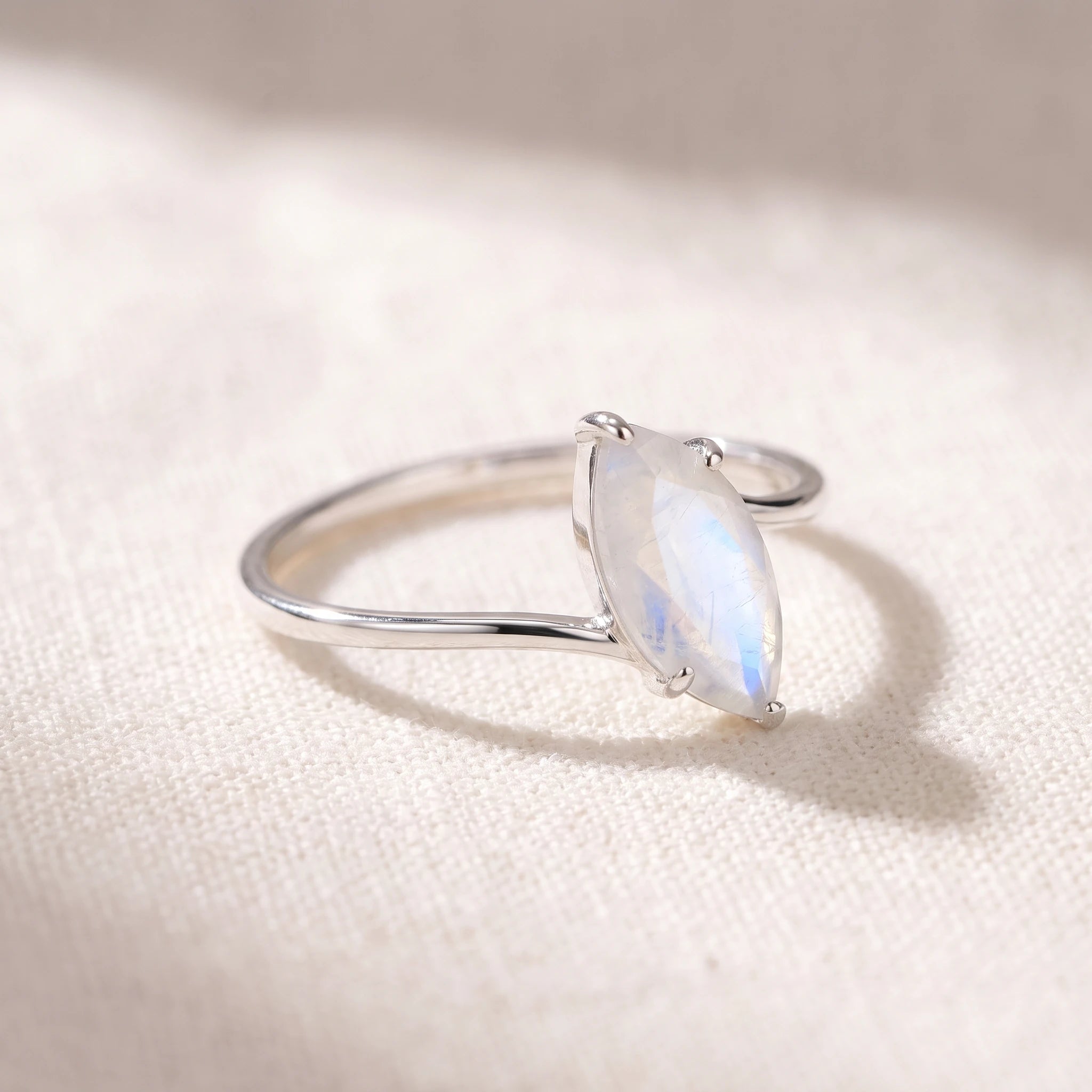 Marquise rainbow moonstone ring at a 45 degree angle on linen, showing the prongs and wrap band