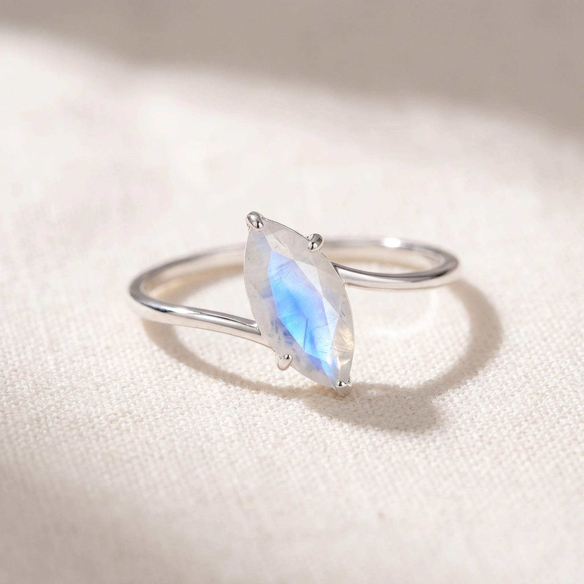 Marquise rainbow moonstone ring flat lay on warm white linen, faceted moonstone on a silver wrap band
