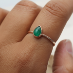 Rose Gold ring with a green tear drop shaped natural emerald gemstone on a person's finger against a neutral background