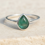 sterling Silver ring with a green teardrop-shaped natural emerald gemstone on a beige background